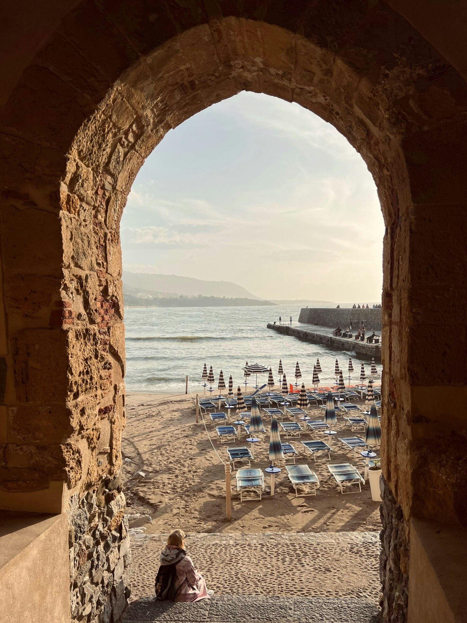 A person sitting under a natural rock archway on a beach