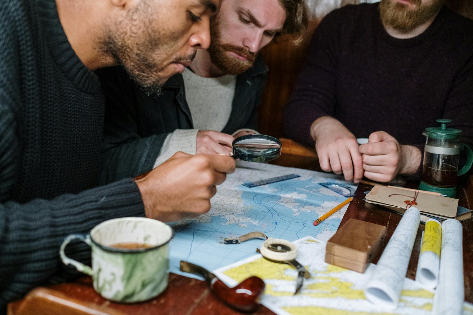 Three men are intensely discussing plans using maps and a magnifying glass, creating a scene of collaboration.